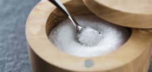 Wooden salt container with a metal spoon, showcasing coarse white salt inside. Ideal for culinary use and kitchen decor.