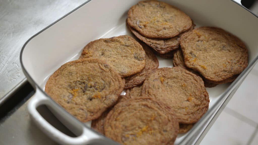 Freshly baked chocolate chip cookies arranged in a white baking dish, showcasing a golden-brown color and a slightly crispy texture. Ideal for dessert lovers and home bakers.