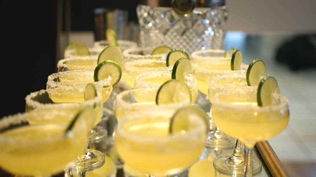 A row of margarita cocktails garnished with lime slices and salt rims, displayed elegantly on a reflective surface, ideal for festive occasions or summer gatherings.