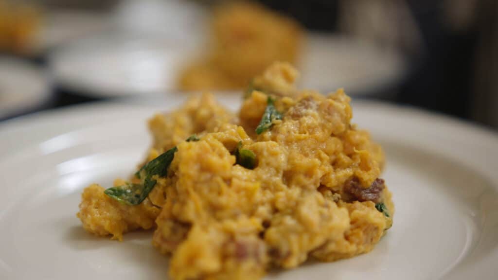 Close-up of a creamy, savory dish featuring scrambled eggs mixed with spinach and bits of sausage, served on a white plate, showcasing a rich texture and vibrant colors.