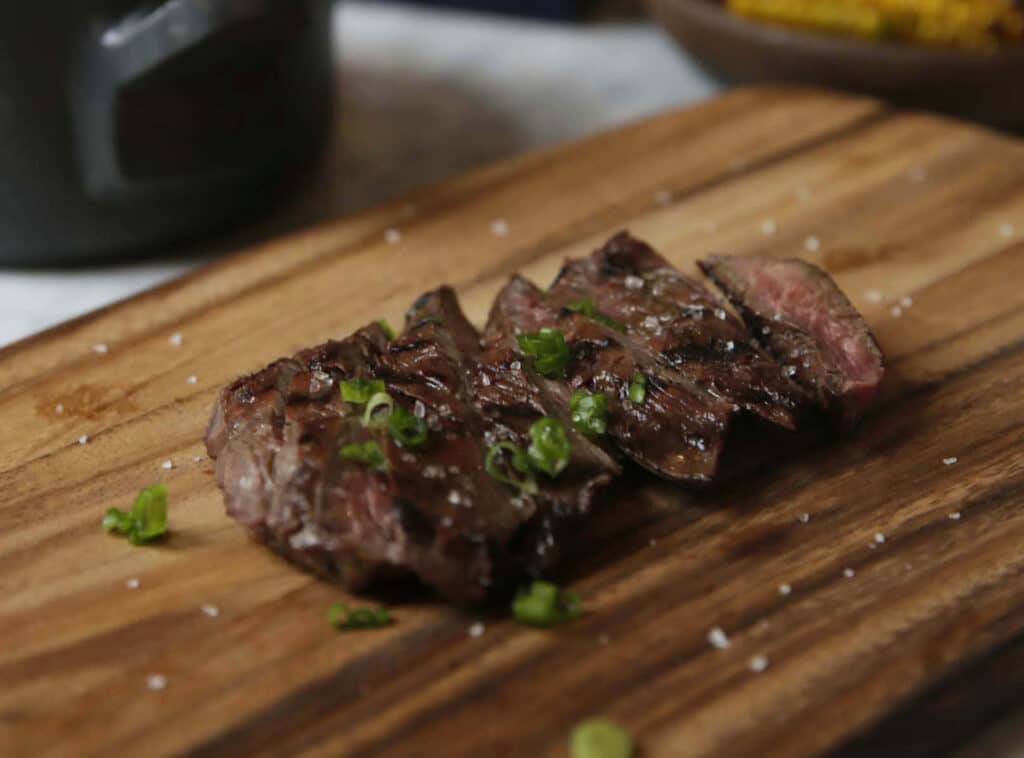 Grilled steak slices garnished with green onions, served on a wooden cutting board, showcasing a delicious and savory dish.