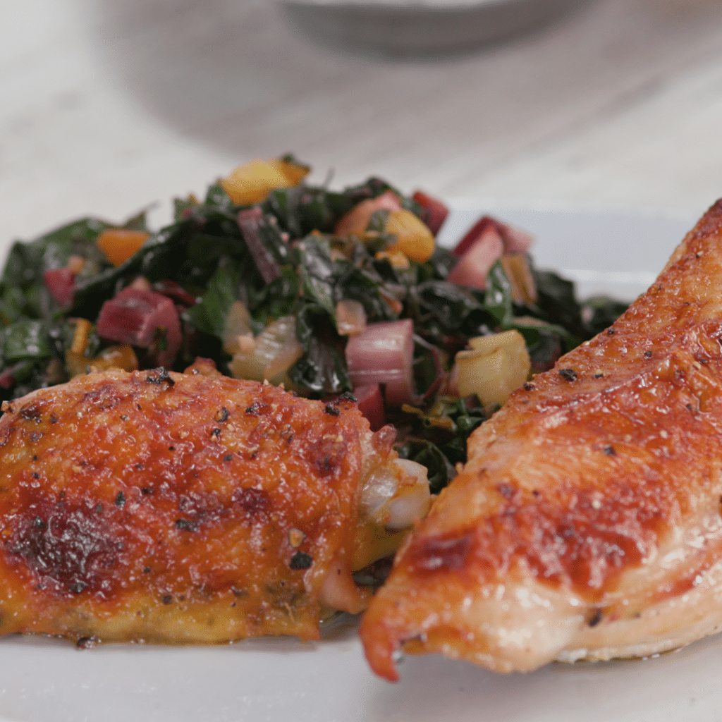 Crispy roasted chicken thighs served alongside sautéed rainbow chard and colorful vegetables on a white plate, highlighting a healthy and flavorful meal option.