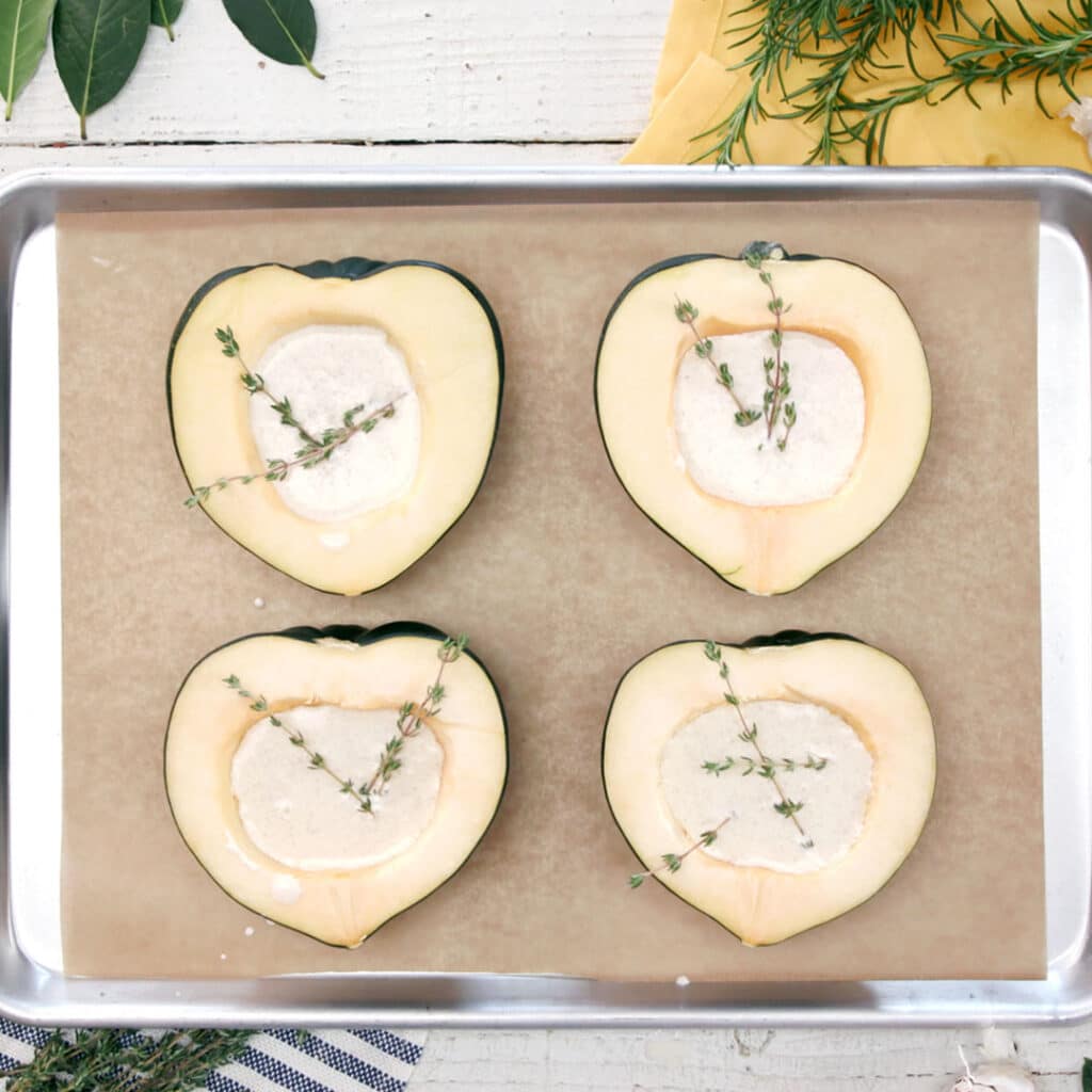 Baked acorn squash halves filled with creamy mixture and garnished with fresh thyme, arranged on a baking sheet lined with parchment paper.