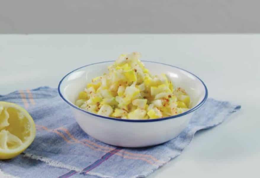 Bowl of fresh chopped vegetables, including yellow squash and potatoes, seasoned and served on a blue cloth with a halved lemon. Ideal for healthy meal options and side dishes.