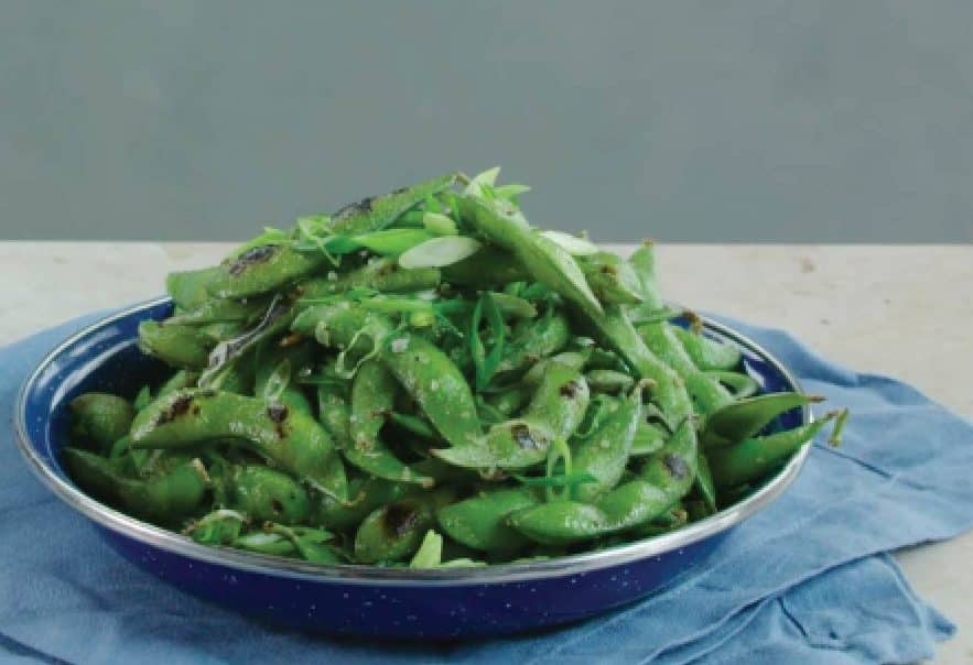 Plate of steamed edamame sprinkled with green onions, served on a blue cloth background, showcasing a healthy and vibrant snack option.