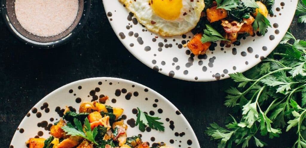 Colorful breakfast plates featuring sautéed vegetables, topped with fresh herbs and a sunny-side-up egg, accompanied by a small bowl of salt. Ideal for healthy meal inspiration.