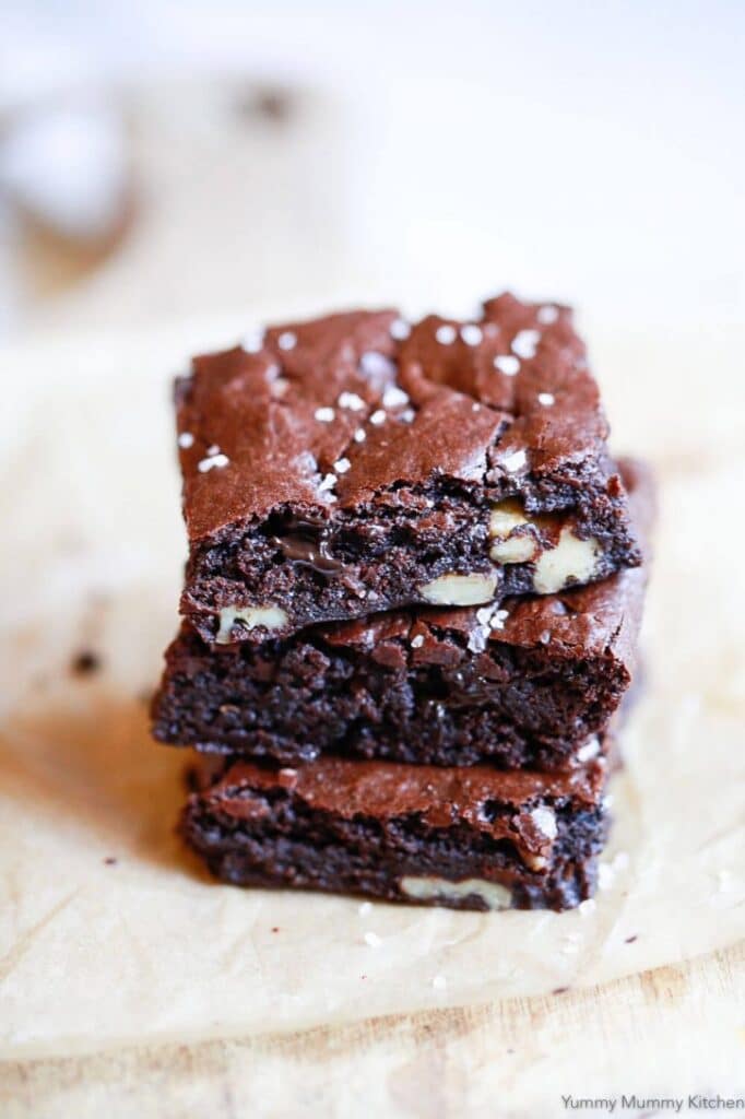 Deliciously fudgy chocolate brownies stacked on parchment paper, featuring chunks of walnuts and a sprinkle of sea salt on top. Perfect for dessert lovers and a great addition to any baking recipe collection.