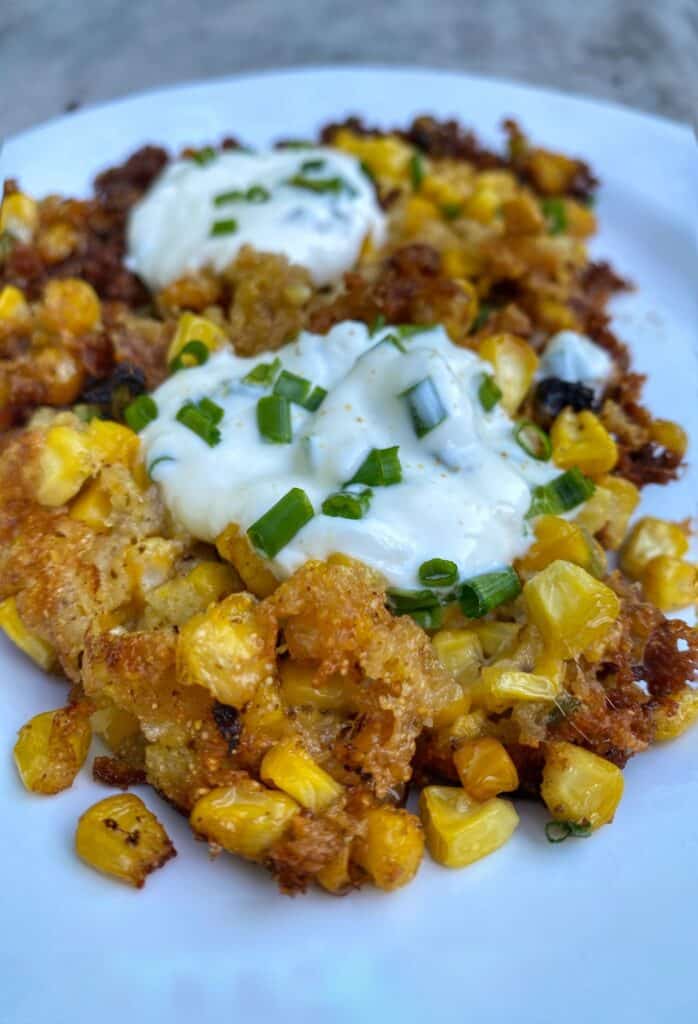 Golden corn fritters topped with creamy yogurt and fresh green onions, served on a white plate.