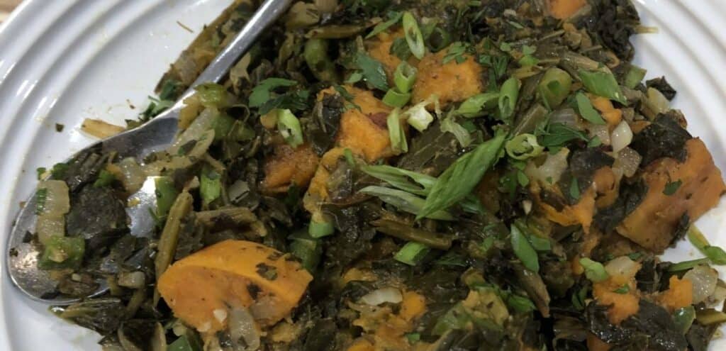 Plate of sautéed greens with sweet potatoes, garnished with chopped green onions and herbs, showcasing a healthy and flavorful dish.