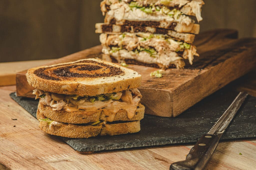 Close-up of a delicious sandwich made with toasted bread, filled with shredded turkey, lettuce, and a creamy sauce, served on a slate plate with a wooden cutting board in the background.