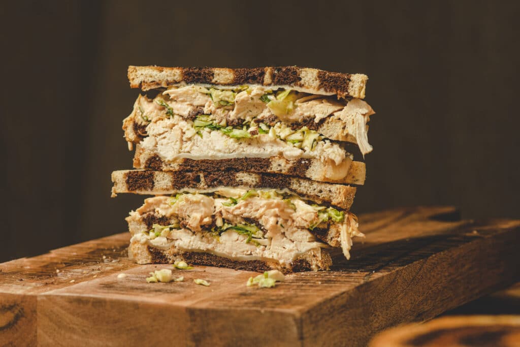 Stacked turkey sandwich with lettuce and creamy dressing on toasted brown bread, displayed on a wooden cutting board.