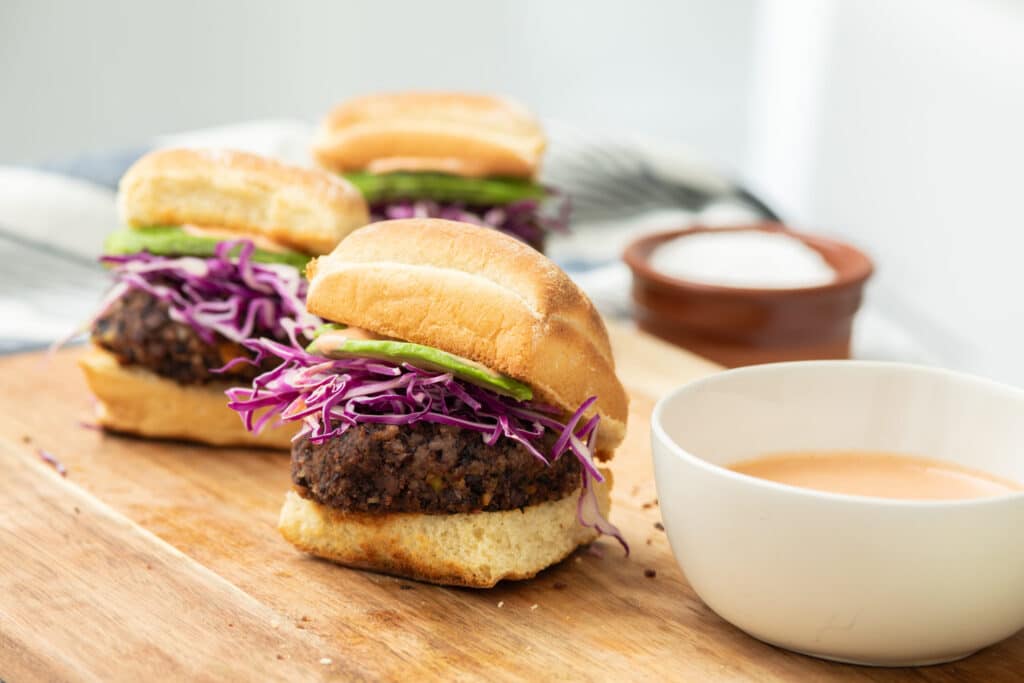 Delicious black bean sliders topped with purple cabbage and green peppers, served on a wooden cutting board alongside a creamy dipping sauce.
