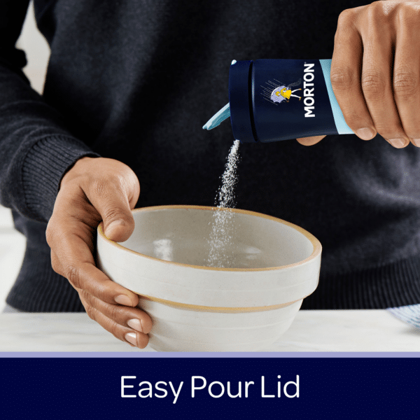 Person pouring salt from a Morton container with an easy pour lid into a white bowl, showcasing a practical kitchen use.