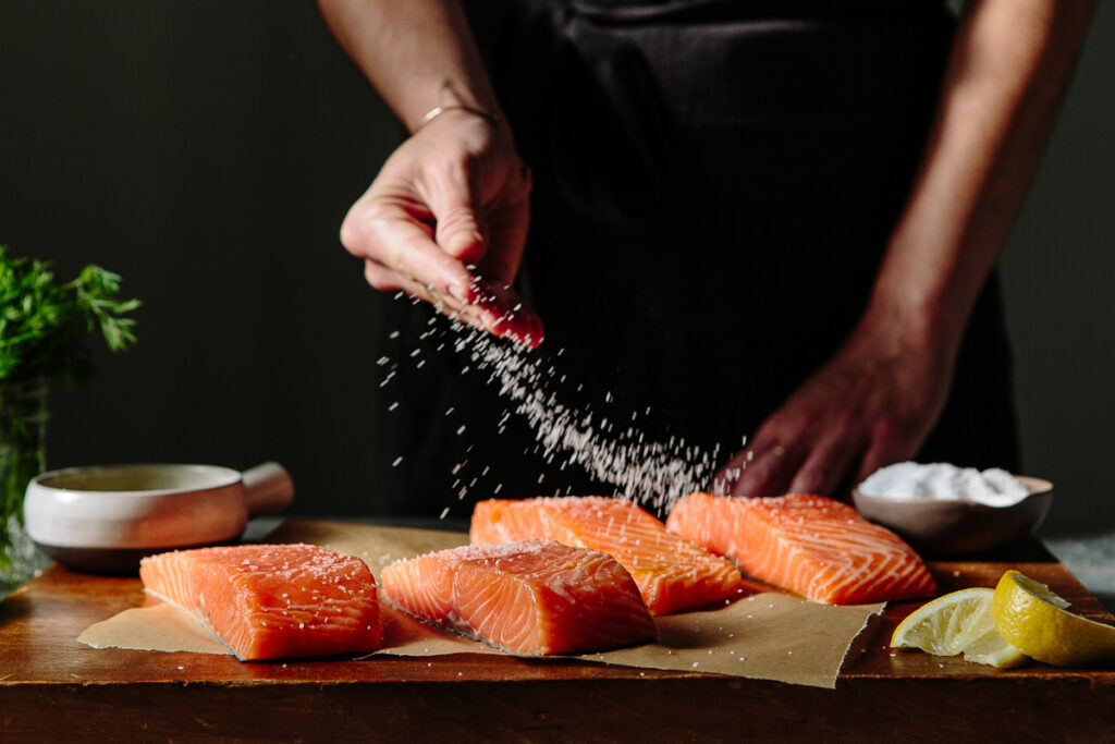 Someone sprinkling salt onto salmon