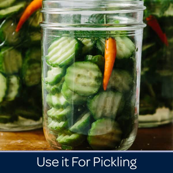 Close-up of jars filled with sliced cucumbers, dill, and a red chili pepper, showcasing homemade pickling ingredients. Ideal for recipes and tips on pickling techniques.