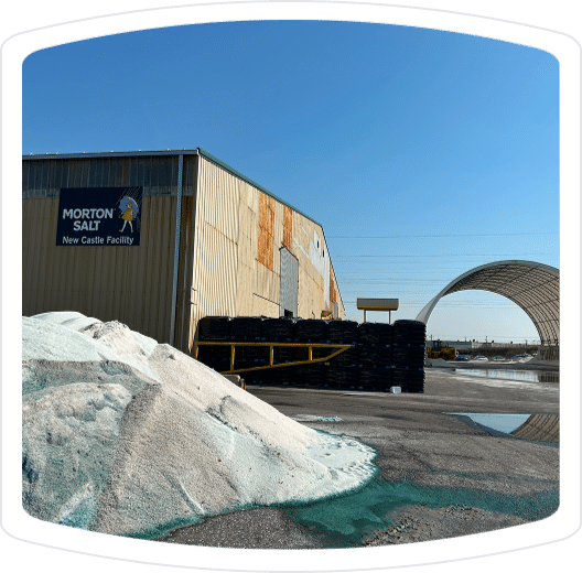 Morton Salt New Castle facility with salt piles in the foreground and storage area visible, under a clear blue sky.