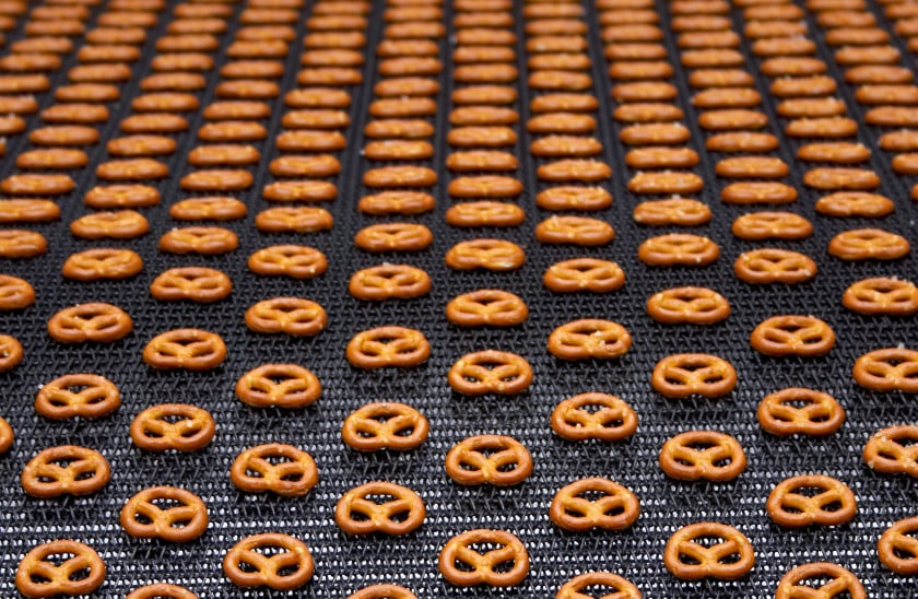 Rows of freshly baked pretzels cooling on a conveyor belt in a snack production facility, showcasing their golden-brown color and traditional shape.