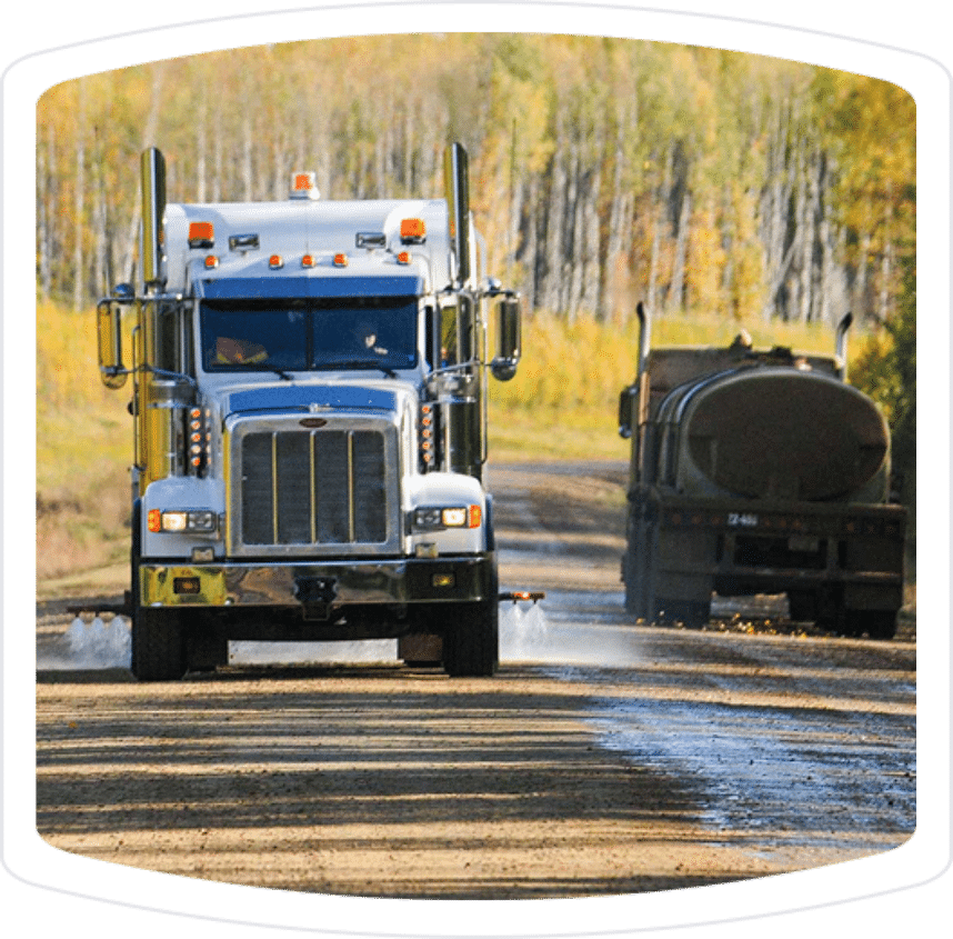 Heavy-duty trucks driving on a gravel road in a rural area, showcasing a Peterbilt truck in the foreground and a tanker truck in the background, surrounded by autumn foliage.