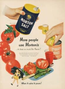 Vintage advertisement featuring Morton Salt, showcasing a hand holding the iconic blue container alongside fresh tomatoes and a glass of tomato juice. The ad emphasizes the flavor-enhancing qualities of Morton Salt, appealing to culinary enthusiasts.