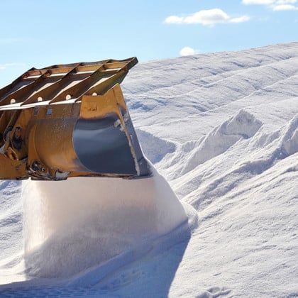 Heavy machinery loading a large pile of white salt against a clear blue sky, demonstrating salt production or storage processes.