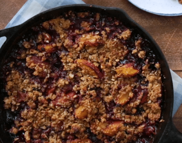 Delicious homemade fruit crisp in a cast iron skillet, featuring a golden oat topping and juicy baked peaches, perfect for dessert lovers and seasonal gatherings.