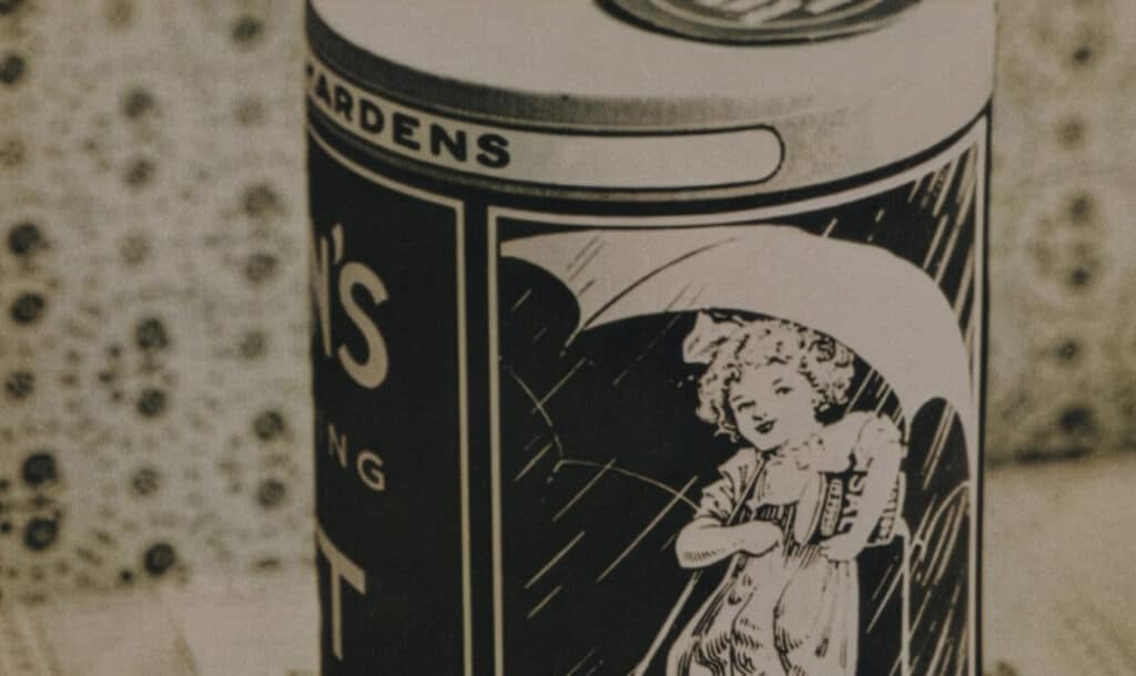 Vintage can featuring a whimsical illustration of a girl holding an umbrella, with a decorative patterned background. The can is labeled with "Garden's" and emphasizes a nostalgic design, highlighting its historical appeal in the context of retro packaging.