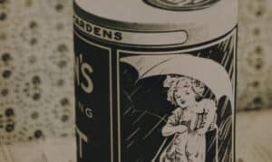 Vintage can featuring a whimsical illustration of a girl holding an umbrella, with a decorative patterned background. The can is labeled with "Garden's" and emphasizes a nostalgic design, highlighting its historical appeal in the context of retro packaging.