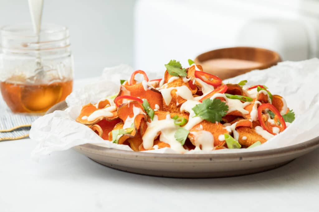 Colorful plate of nachos topped with creamy sauce, sliced jalapeños, green onions, and fresh cilantro, with a jar of honey in the background. Perfect for a delicious snack or appetizer.