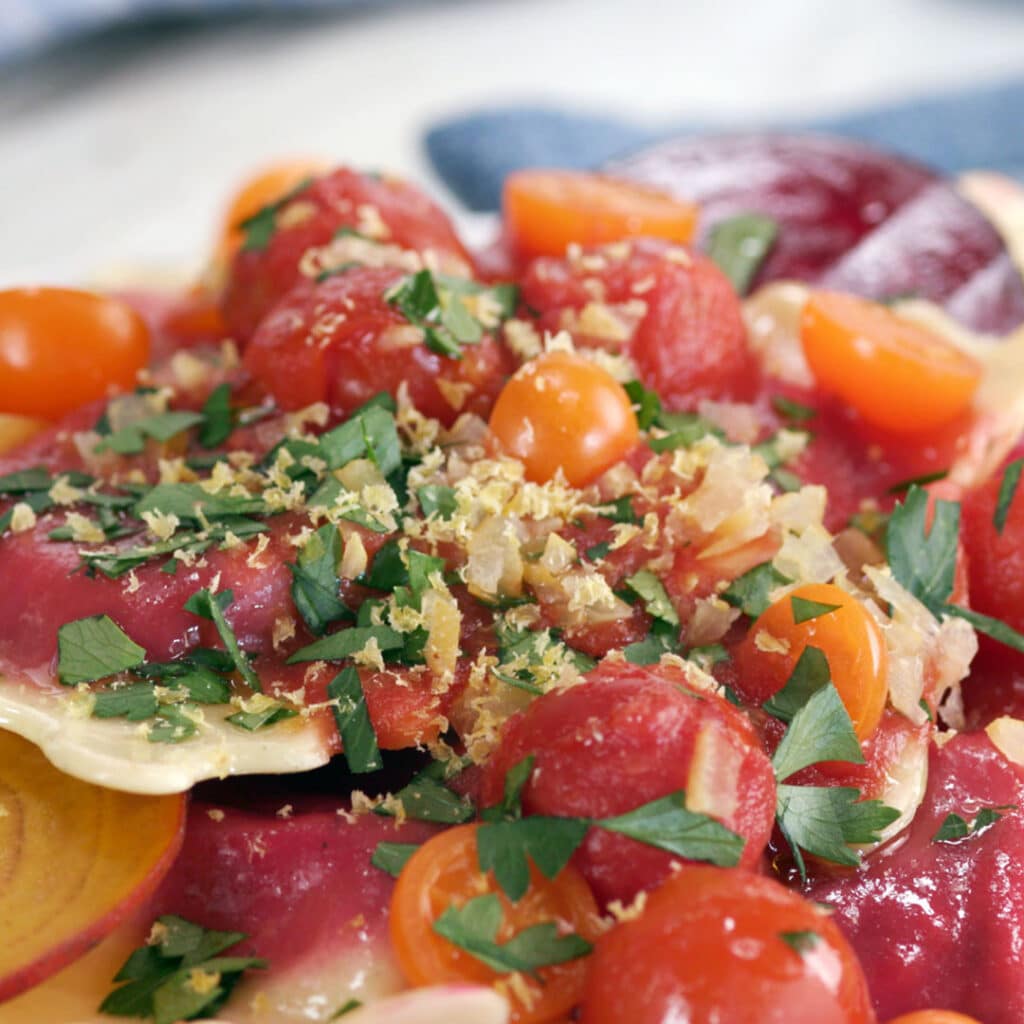 Colorful plate of ravioli topped with fresh tomatoes, herbs, and a sprinkle of lemon zest, showcasing a vibrant and appetizing Italian dish.