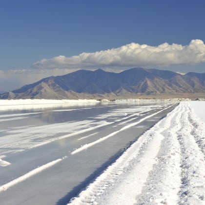 Scenic view of a salt flat with a reflective surface, surrounded by mountains under a clear blue sky, showcasing natural salt formations and a tranquil landscape.