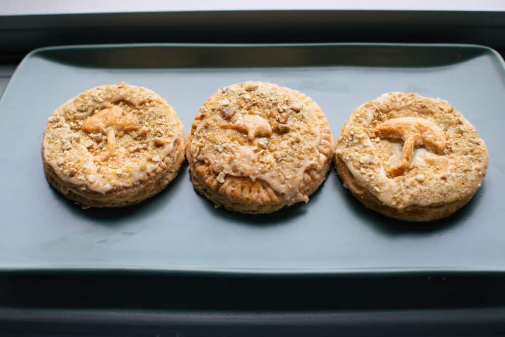 Three delicious pies topped with crushed nuts and icing, displayed on a light blue plate. Each cookie features a unique design, showcasing a variety of textures and flavors. Perfect for dessert lovers and baking enthusiasts.