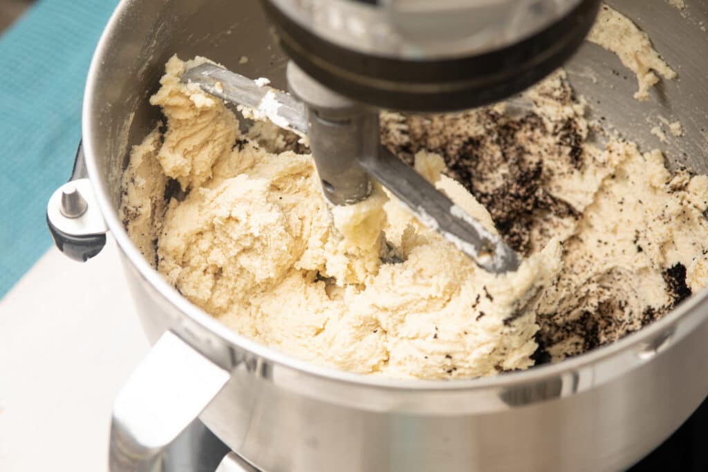 Close-up of cookie dough being mixed in a stand mixer, showcasing a blend of creamy batter and chocolate cookie crumbs, ideal for baking enthusiasts.