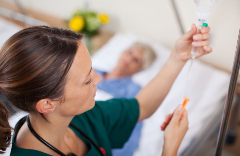 Nurse administering IV medication to a patient in a hospital room, with a focus on patient care and medical treatment.