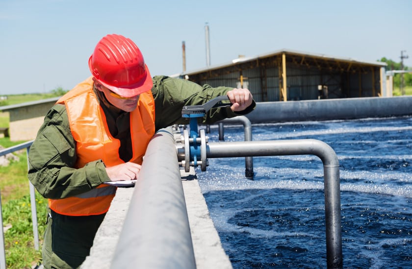 Worker in safety gear inspecting water treatment equipment at a wastewater treatment facility, ensuring proper operation and maintenance of the system.