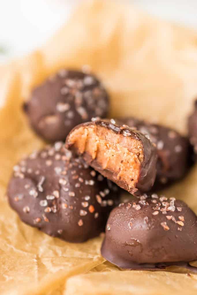 Delicious chocolate-covered treats with a peanut butter filling, topped with sea salt, arranged on parchment paper. One treat is cut in half, showcasing the creamy interior. Perfect for dessert lovers and indulgent snacking.