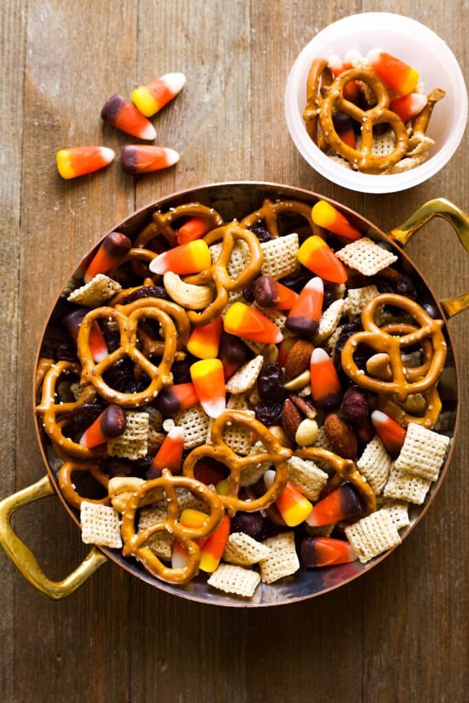 Colorful Halloween snack mix featuring pretzels, candy corn, nuts, and cereal in a bowl, perfect for festive gatherings and parties.