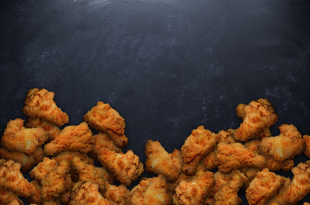 A pile of crispy, golden fried chicken pieces arranged on a dark surface, showcasing their crunchy texture and appetizing appearance, ideal for food photography and culinary blogs.