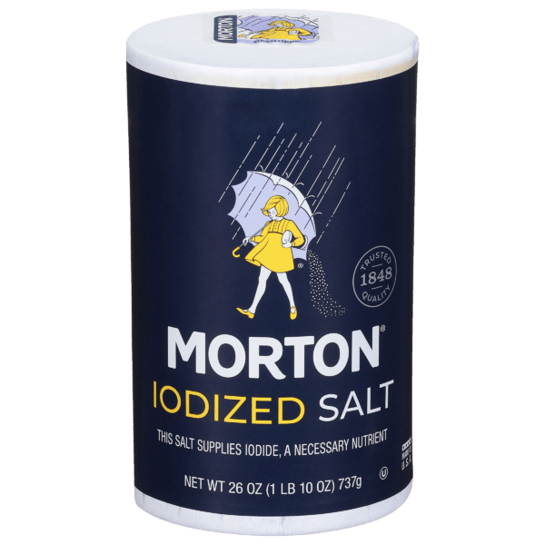 Morton iodized salt container featuring a classic design with a girl in a yellow raincoat holding an umbrella. The label highlights that the salt provides iodine, an essential nutrient, and indicates a net weight of 26 ounces. Trusted quality since 1848.