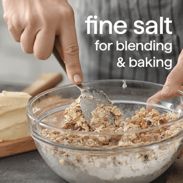 Person mixing oats and flour with fine salt in a glass bowl, with butter on a wooden board in the background, highlighting ingredients for baking and blending.