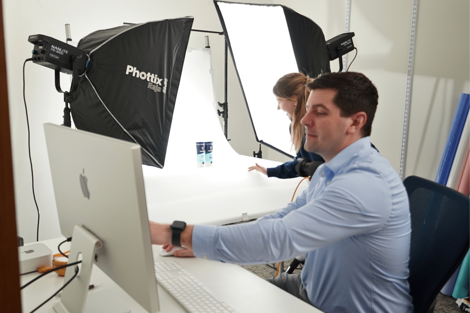 photo shoot is happening there are light shining on the products with a person pointing at a computer screen.