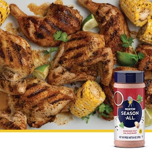 Grilled chicken pieces seasoned with Morton Season-All, accompanied by corn on the cob and lime wedges, showcasing a flavorful summer meal.