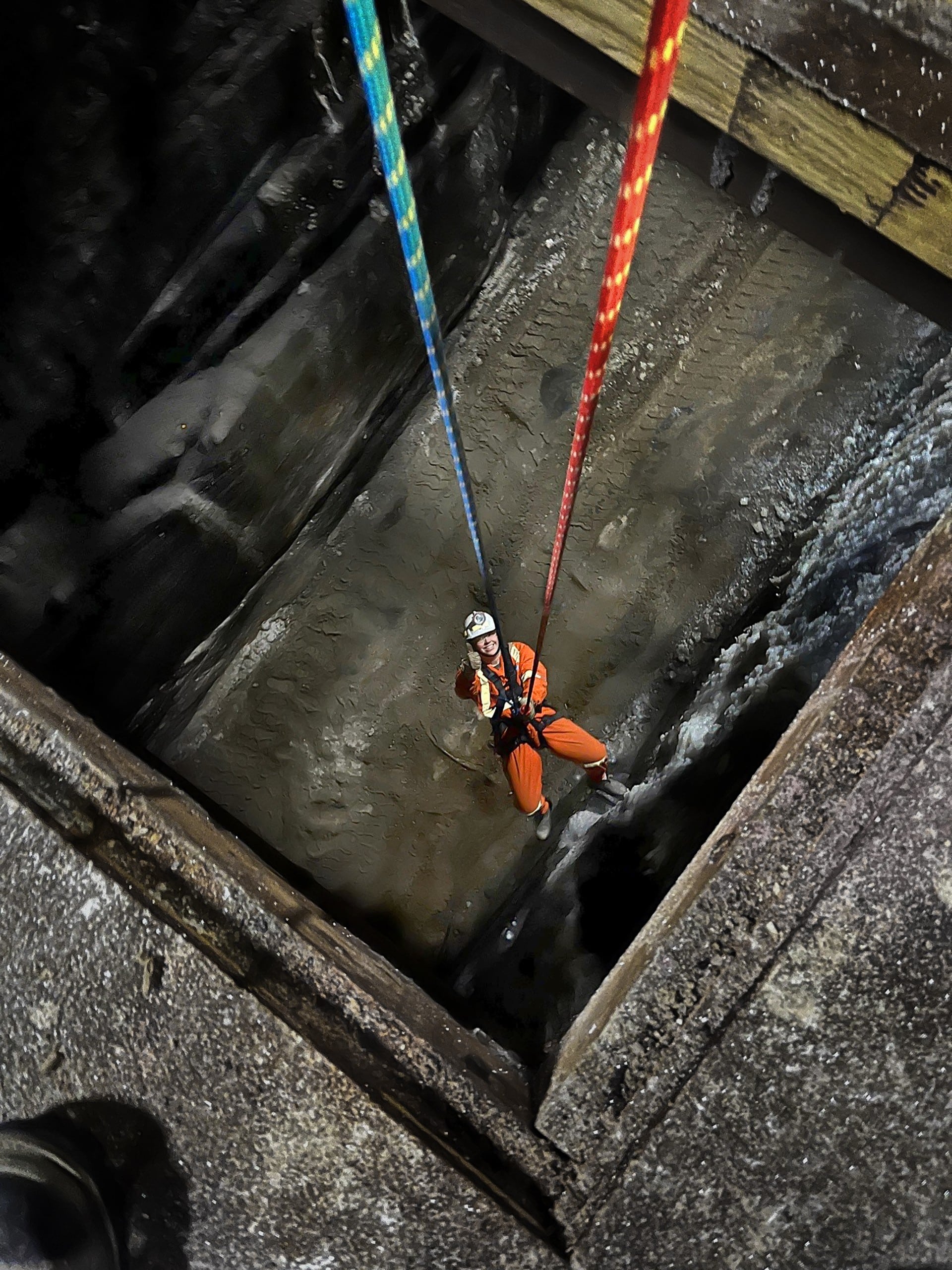 Une personne en tenue de sécurité descend en rappel dans un puits profond et sombre à l'aide de cordes colorées, illustrant ainsi les techniques de sauvetage industriel et les mesures de sécurité en action.