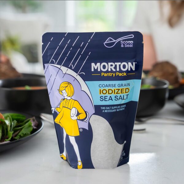 Morton Coarse Grain Iodized Sea Salt Pantry Pack displayed on a kitchen countertop, with a salad and other dishes in the background, highlighting its nutritional benefits and convenient packaging.