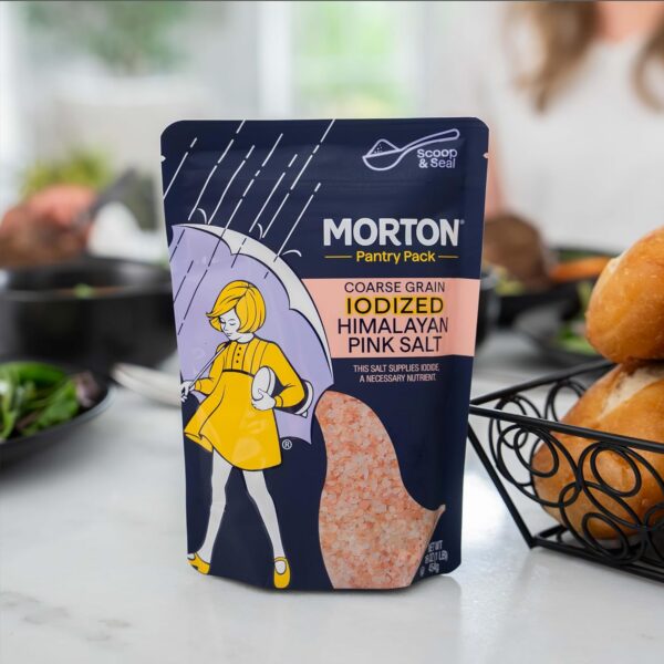 Morton Pantry Pack coarse grain iodized Himalayan pink salt in a colorful pouch, displayed on a kitchen countertop with a salad and bread rolls in the background, highlighting its nutritional benefits.