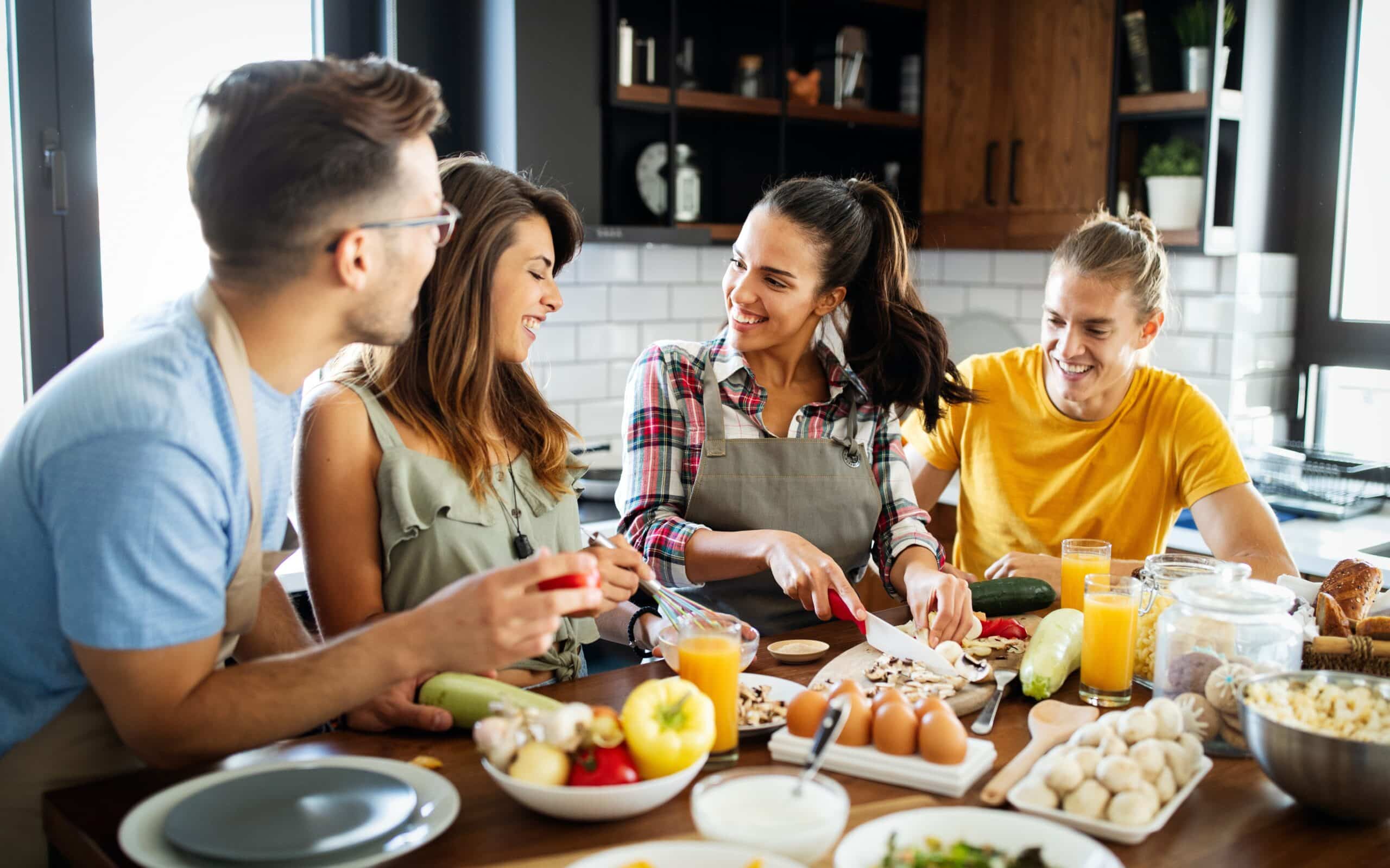 Group of friends enjoying a cooking session in a modern kitchen, preparing healthy meals together with fresh ingredients, including vegetables, fruits, and eggs, while sharing laughter and conversation.
