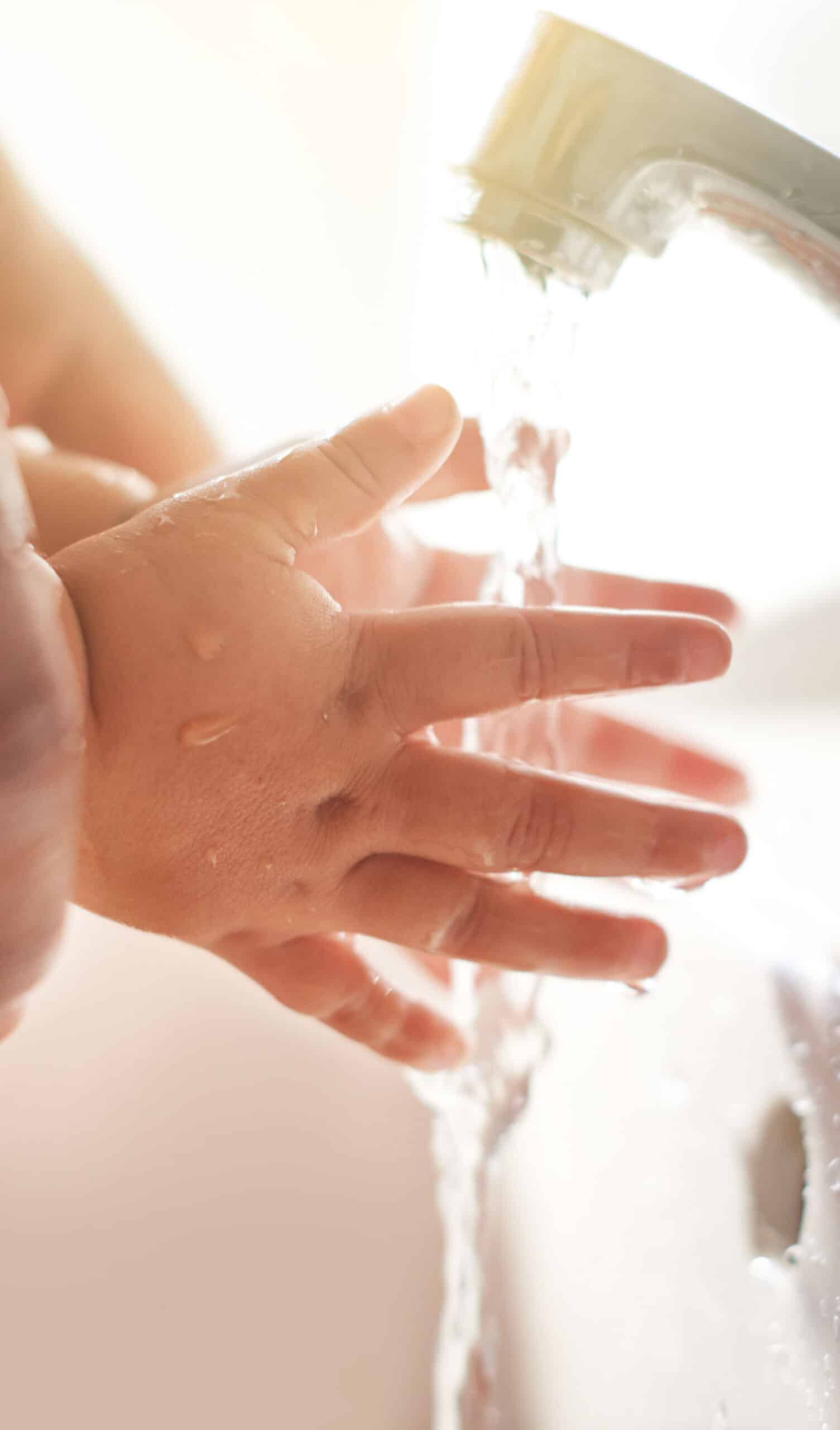 Close-up of a child's hand under running water from a faucet, emphasizing the importance of handwashing for hygiene and health.