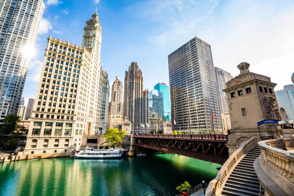 La silhouette de Chicago, avec son architecture historique le long du fleuve, notamment l'emblématique Wrigley Building et la Tribune Tower, ainsi qu'un pont enjambant les eaux turquoise, témoigne du riche patrimoine et du développement moderne de la ville.